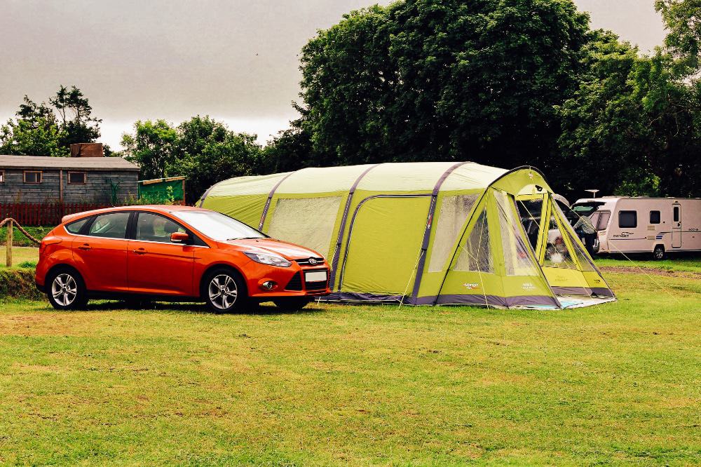 A large family tent at a campsite with a car 