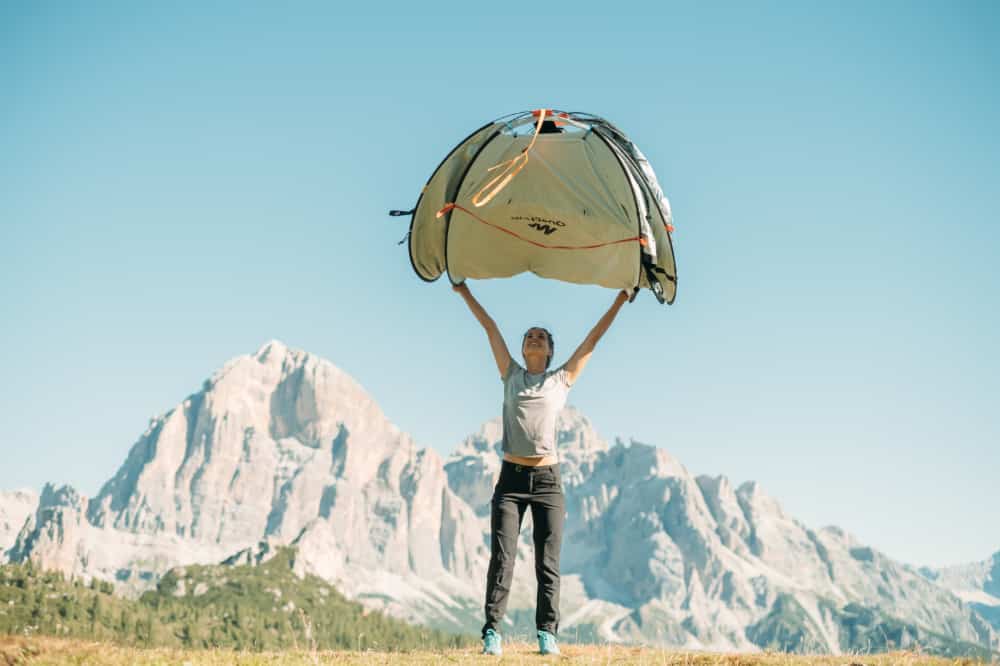 Woman on a mountain plateau about to release a pop up tent to open up.